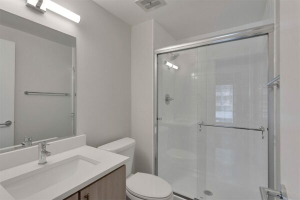 Bathroom with white counter and sink, large mirror, modern light fixture, and tiled shower with glass door.