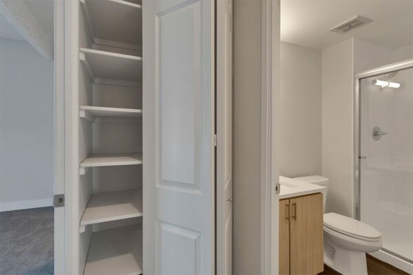 Bathroom with wood cabinet and white counter and closet with built in shelves.