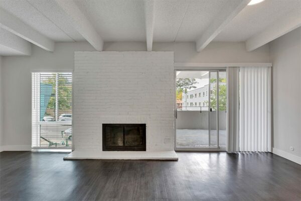 Living room with wood floor, white brick accent wall with fireplace, and door to balcony.