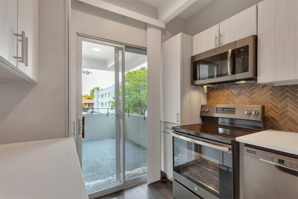 Kitchen with light cabinets and counters, stainless steel appliances, tiled backsplash, and door to balcony.