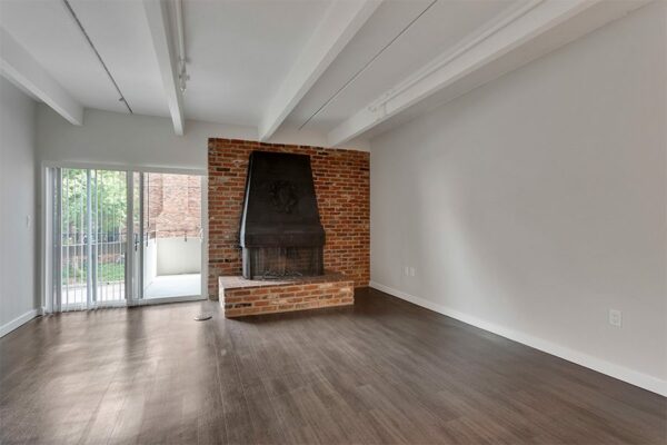 Living room with wood floor, brick accent wall with fireplace, and door to balcony.