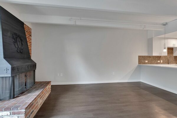 Living area with wood floor, grey walls, brick accent wall with fireplace, and modern kitchen.