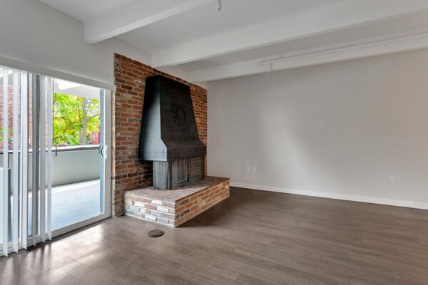 Living room with wood floor, brick accent wall with fireplace, and door to balcony.