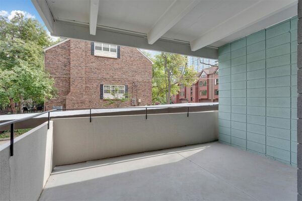 Balcony with concrete walls overlooking street and nearby houses with tall trees.