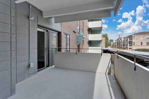 Balcony with concrete walls overlooking covered parking and nearby houses.