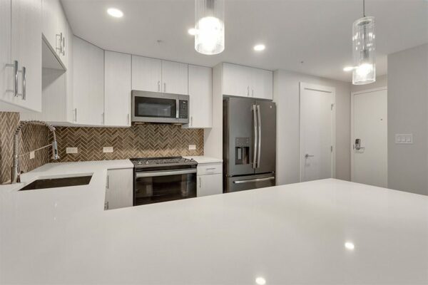Kitchen with light cabinets and counters, stainless steel appliances, tiled backsplash, and breakfast bar with pendant lights.