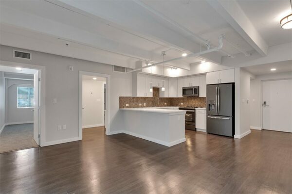 Living area with wood floor, grey walls, doors to bedroom and hallway, and updated kitchen.