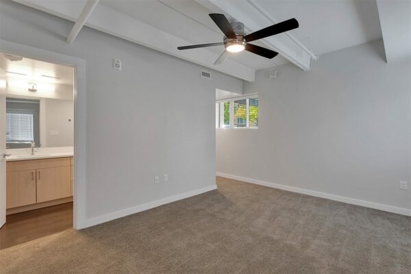Bedroom with carpet, grey walls, ceiling fan, and door to bathroom.