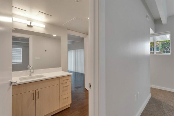 Bathroom with wood floor and cabinets, light counter, and large mirror.