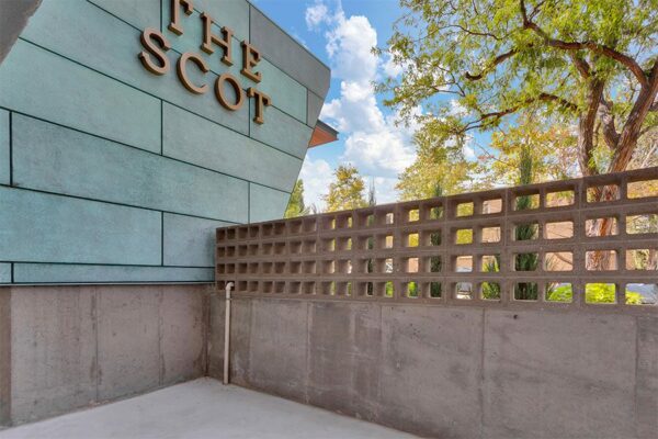 Balcony with decorative cinder blocks and The Scot metal signage under tall trees.