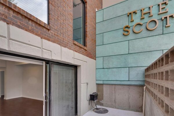 Balcony with decorative cinder blocks, The Scot metal signage, and sliding door to apartment.