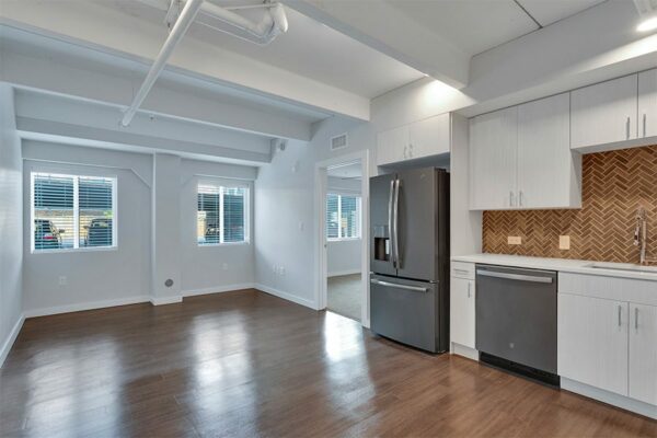 Living area with wood floor, grey walls, large windows, and updated kitchen.