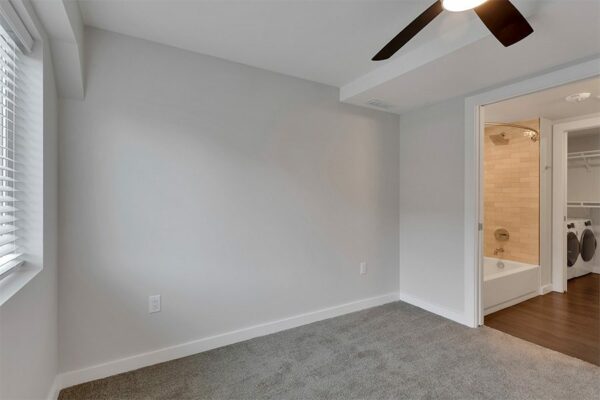 Bedroom with carpet, grey walls, white trim, ceiling fan, and door to bathroom.
