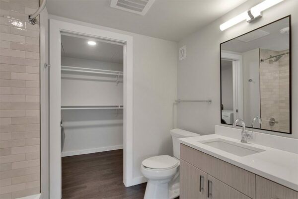 Bathroom with wood floor and cabinets, framed mirror, tiled shower tub, and door to closet.