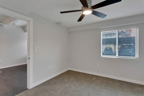Bedroom with carpet, grey walls, white trim, ceiling fan, and door to living room.