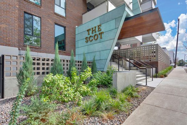 The Scot apartments with lush landscaping, large metal monument sign, and patio.