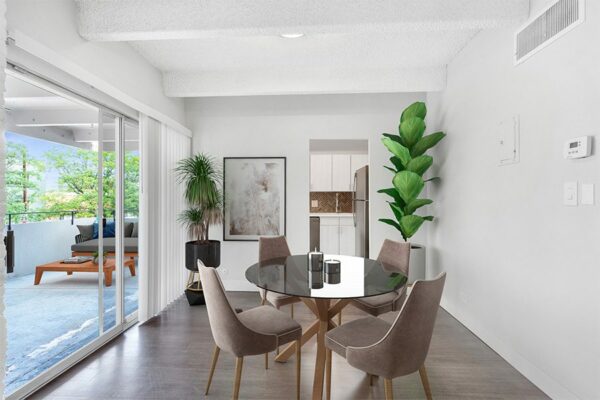 Dining room with wood floor, sliding glass door to balcony, modern dining table, and large potted plants.