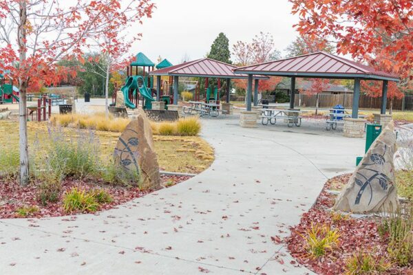 Park with large rock signs, lush landscaping, gazebos with tables, and play equipment.