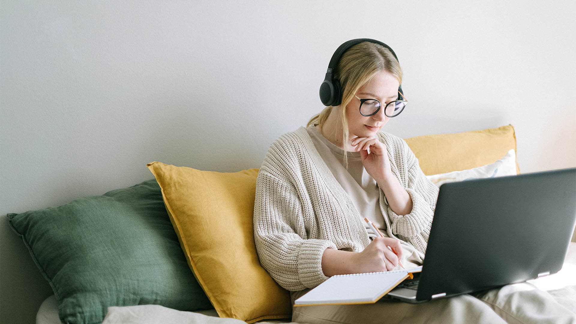 Person sitting on couch working on laptop and notebook.
