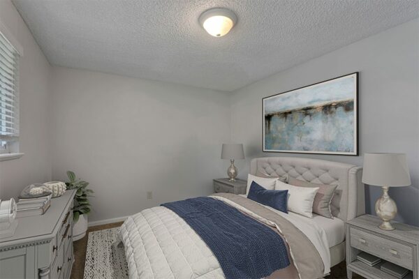 Bedroom with rug, bed with plush headboard and artwork.