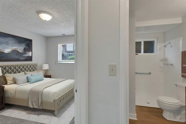 Bedroom with rug, bed with plush headboard, artwork, bathroom and window.