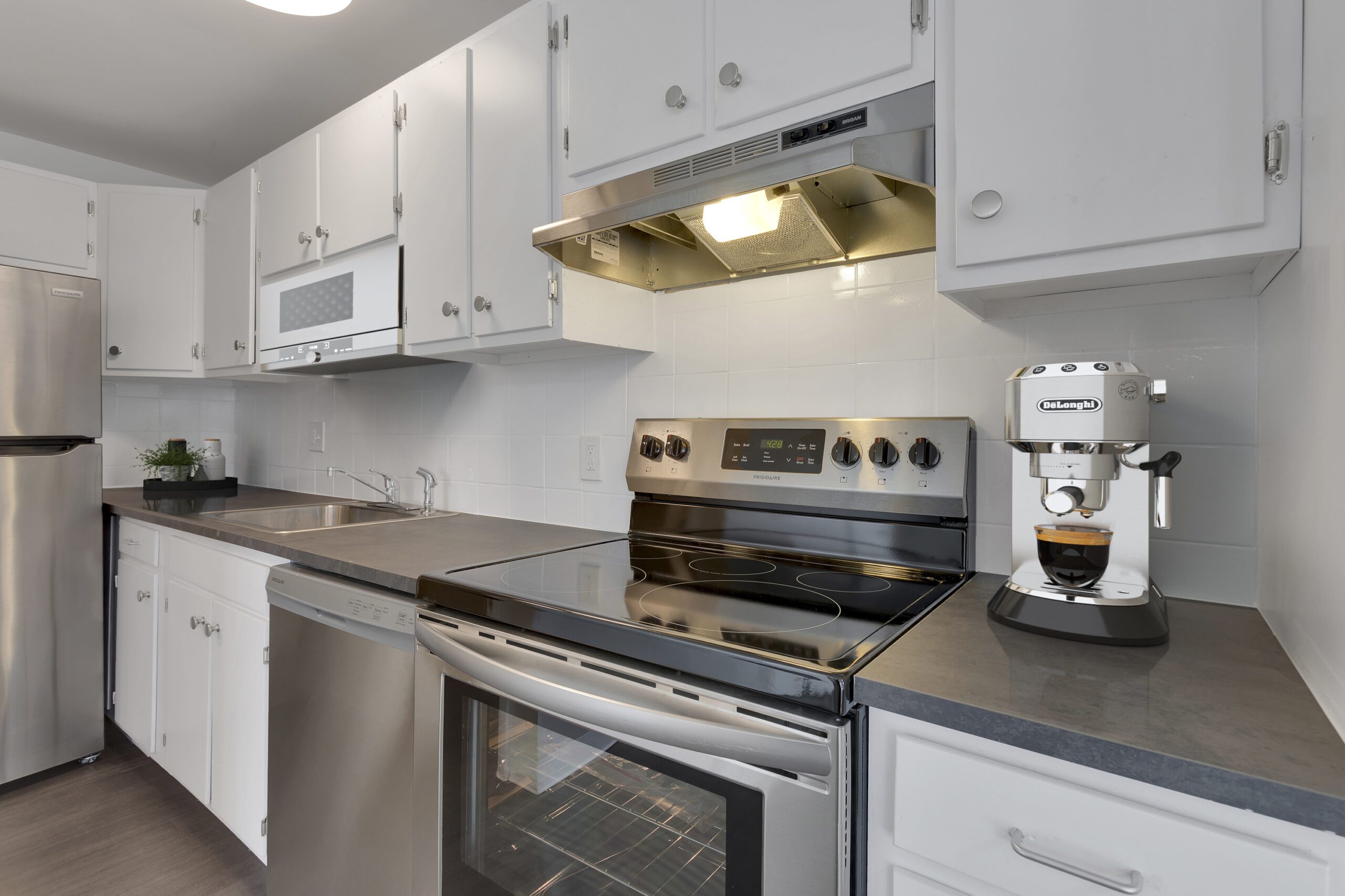 Kitchen with wood floor, white cabinets, grey counters, and stainless steel appliances.