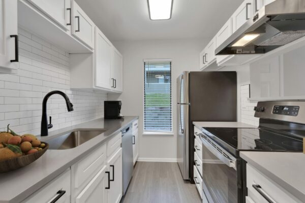 Kitchen with wood floor, white cabinets, stainless steel appliances, and tiled backsplash.