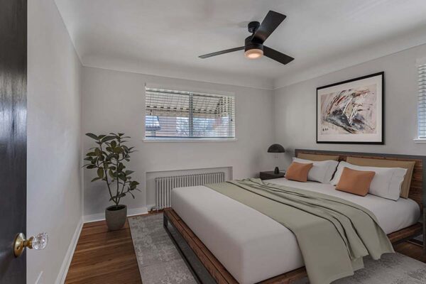 Furnished bedroom with carpet over wood floors, white walls, and a ceiling fan.