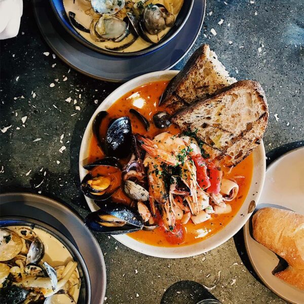 Plates of Italian dishes with shellfish and bread on stone table.