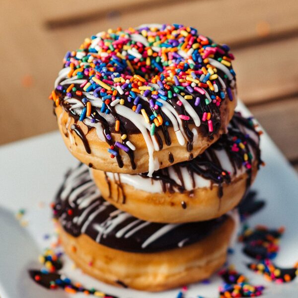 Detail of 3 donuts with frosting and colorful sprinkles stacked on white plate.