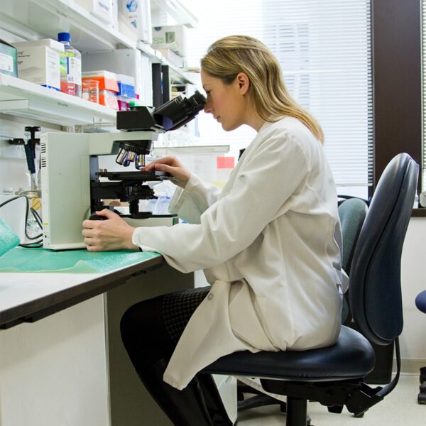 Doctor with long blonde hair in lab coat examining slides with a microscope.