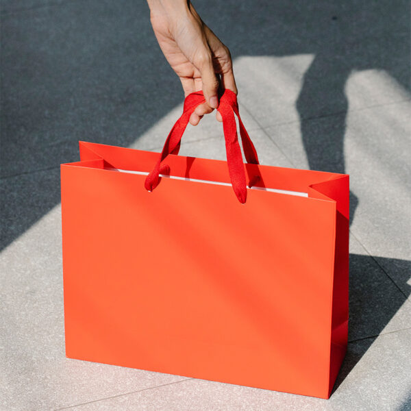 Person holding bright red shopping bag on concrete sidewalk.