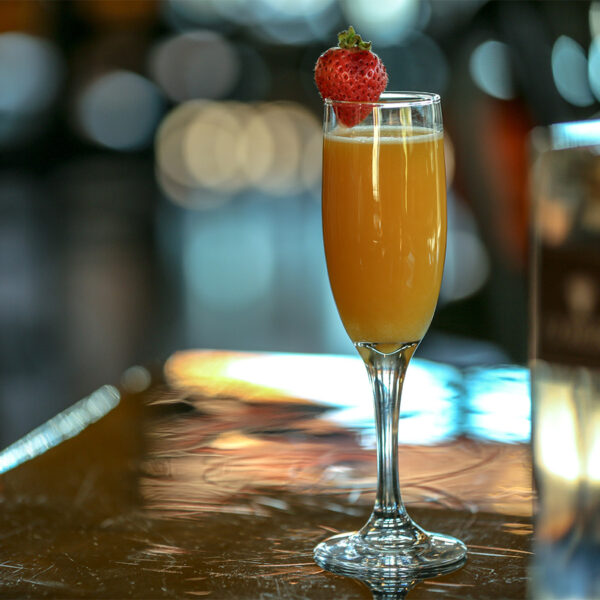 Mimosa in champagne flute with strawberry on table with out of focus lights behind.