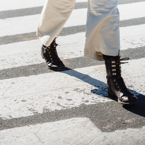 Person in white pants and tall leather boots walking across striped crosswalk.