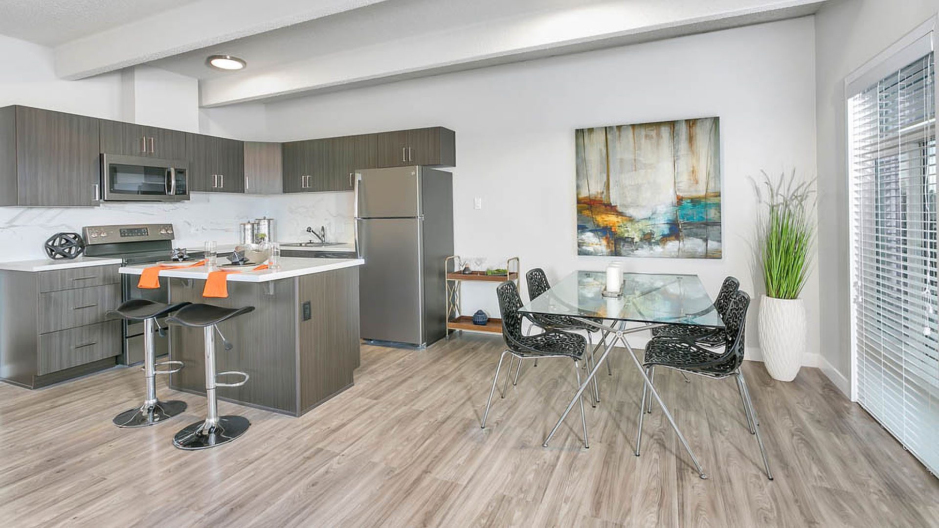 Kitchen and dining with wood floor and cabinets, light counters, stainless steel appliances, and modern dining table.