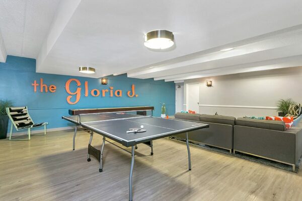 Club room with wood floor, plush couch, table tennis, shuffleboard, and blue accent wall with 
