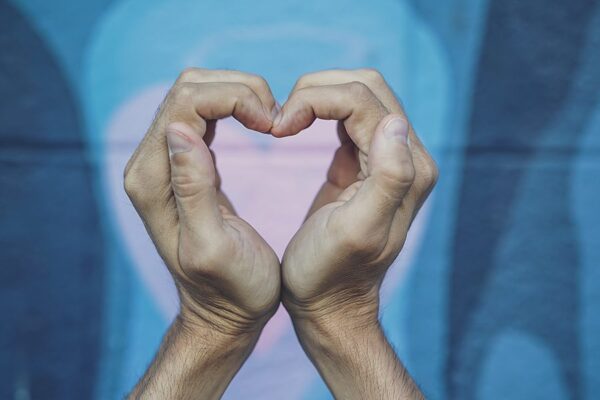 Person holding hands in heart shape in front of wall mural with painted heart.