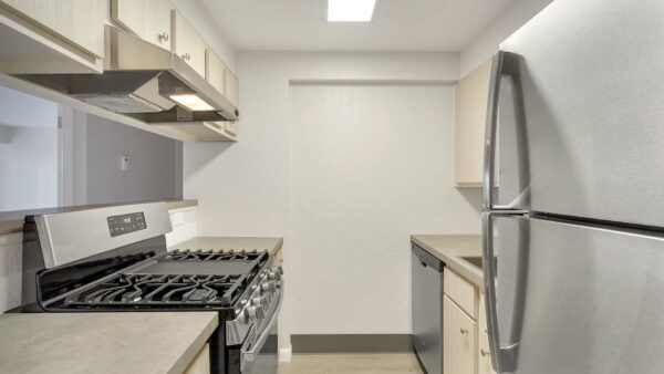 Kitchen with light cabinets and counters, stainless steel appliances, and opening to living room.