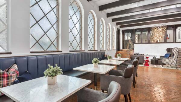 Lounge with brick floor, plush booths with tables and modern chairs, and classic styled windows.