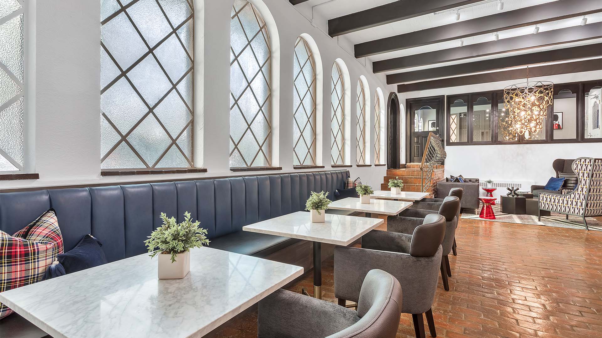 Lounge with brick floor, plush booths with tables and modern chairs, and classic styled windows.