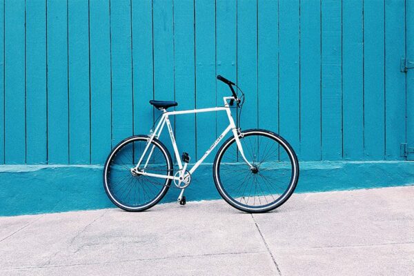 Single speed bike leaning against bright blue painted fence.