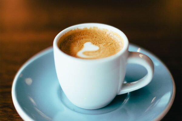Detail of cappuccino with light blue saucer on dark wood table.