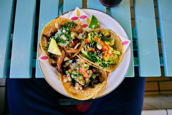 Plate of tacos with meat and vegetables on bright blue wood table.