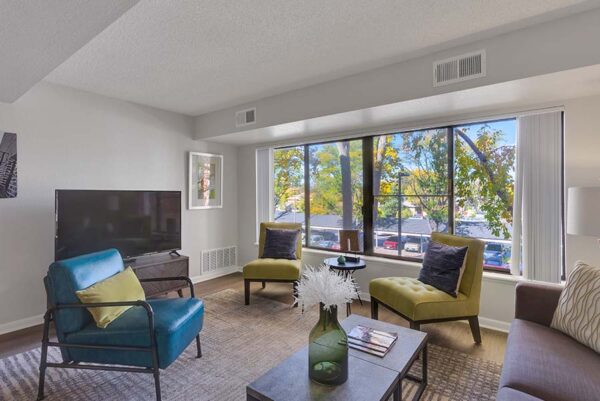 Furnished living room with white walls, large windows, and artwork on the walls.