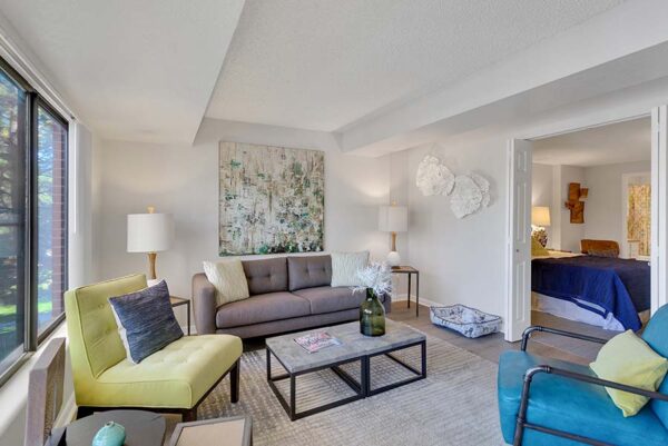 Furnished living room with white walls, large windows, and artwork on the walls.
