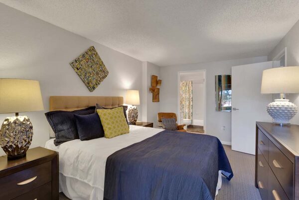 Furnished bedroom with white walls, tan carpet, and artwork on the walls.