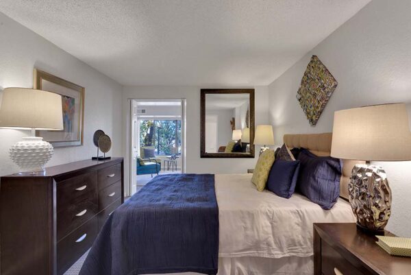 Furnished bedroom with white walls, tan carpet, and artwork on the walls.