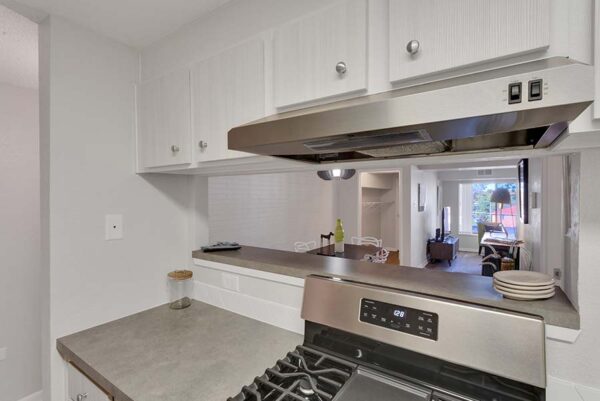 The kitchen showing the oven overlooking the living room, with white cabinets, and gray countertops.