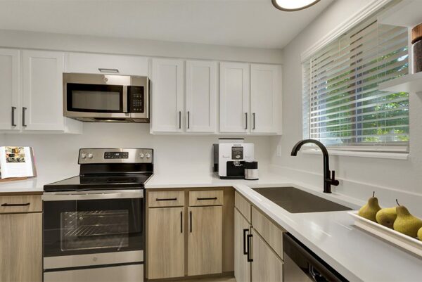 Kitchen with white countertops, stainless steel appliances, white overhead cabinets, and tan lower cabinets.
