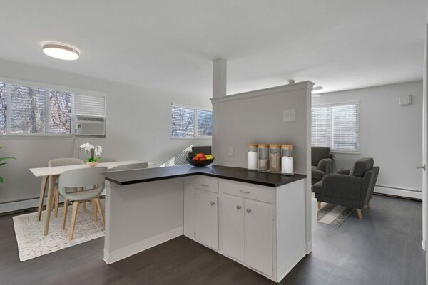 Rendering of an open-concept dining room, kitchen, and living room with gray flooring, white walls, and white cabinets.